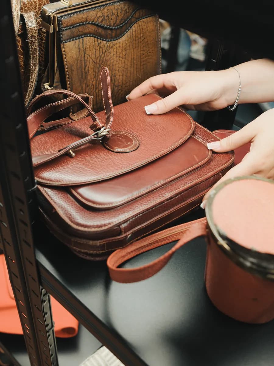 Mani che sfogliano borse in pelle vintage su uno scaffale